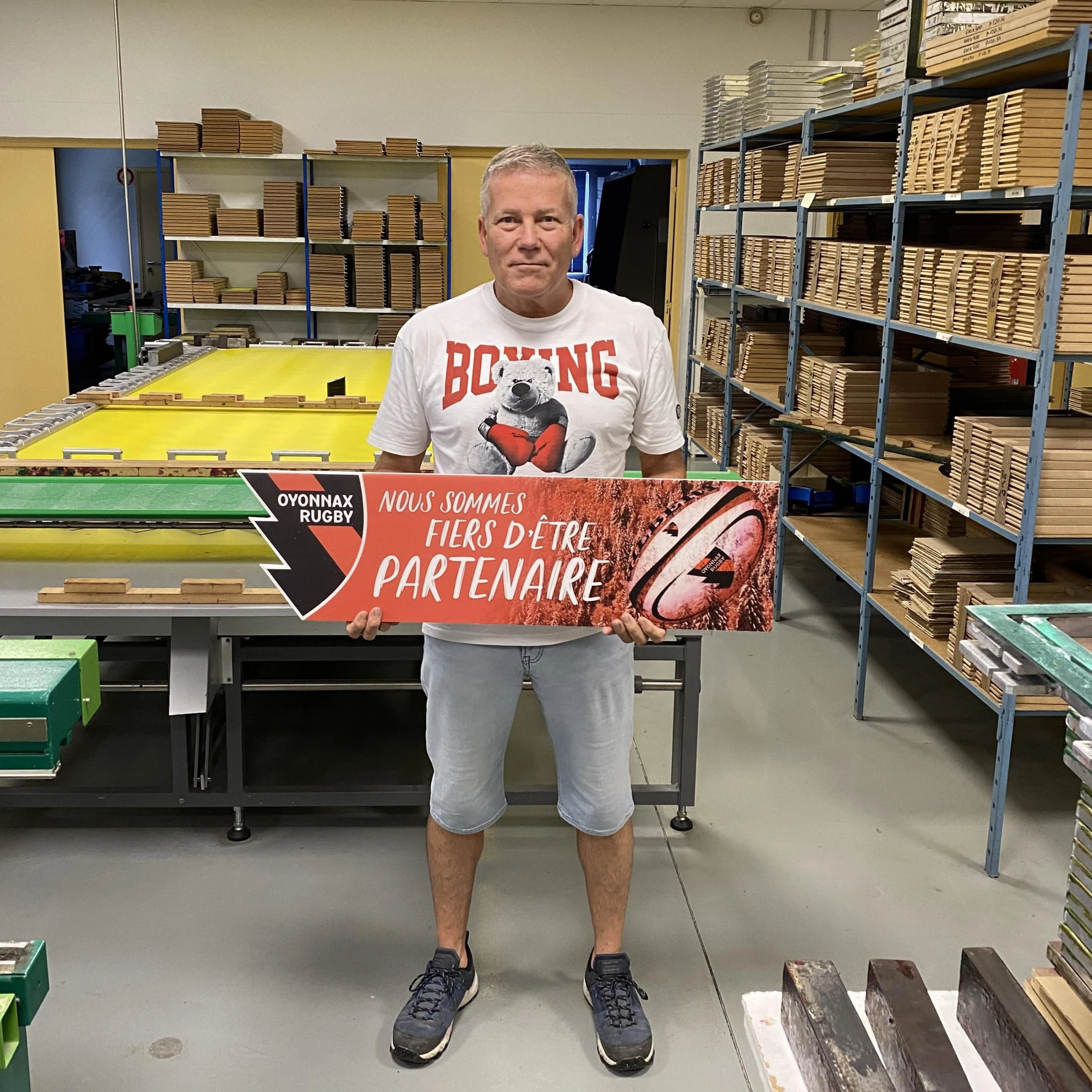 Dans l’atelier, une personne présente un panneau de partenaire Oyonnax Rugby